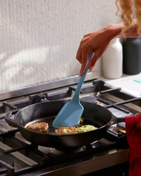 A hand holding the GIR Ultimate Light Blue Flip to flip patties on a frying pan. 