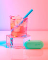 A GIR Kids Straw in a glass of juice with ice on a pink background. 