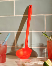 The Red Ladle resting on a marble background with a glass of juice on either side.  