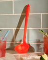 The Red Ladle resting on a marble background with a glass of juice on either side.  