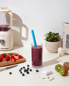 A Smoothie & Boba Straw inside a smoothie on a white background with fruits and other kitchen equipment around it. 
