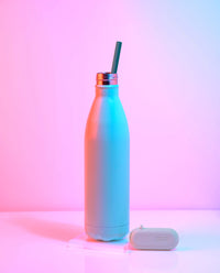 A GIR travellers Straw inside a water bottle on a pink background. 