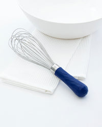The Navy Ultimate Whisk resting on a white kitchen towel next to a white bowl.