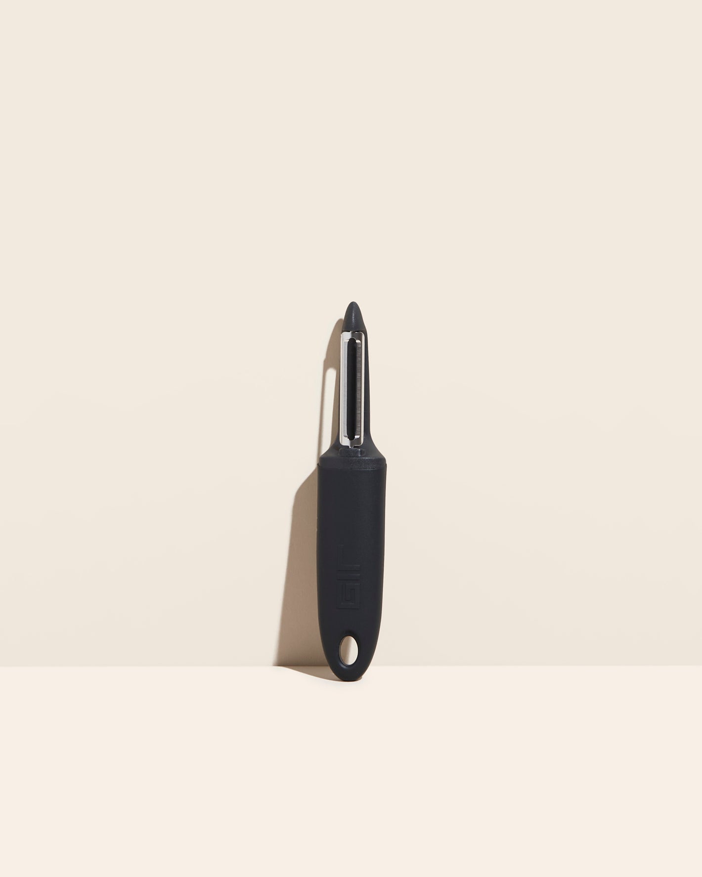  The I Handle Flat Peeler in Black on a cream background. 